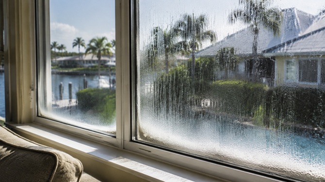 Fogged residential window overlooking Florida waterfront home, condensation obscuring exterior view.
